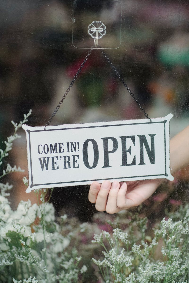 A welcoming open sign in a flower shop window with delicate blossoms in the foreground.